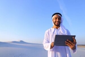 Man wearing a white thawb and izaar while standing in a cool desert and holding a tablet phone